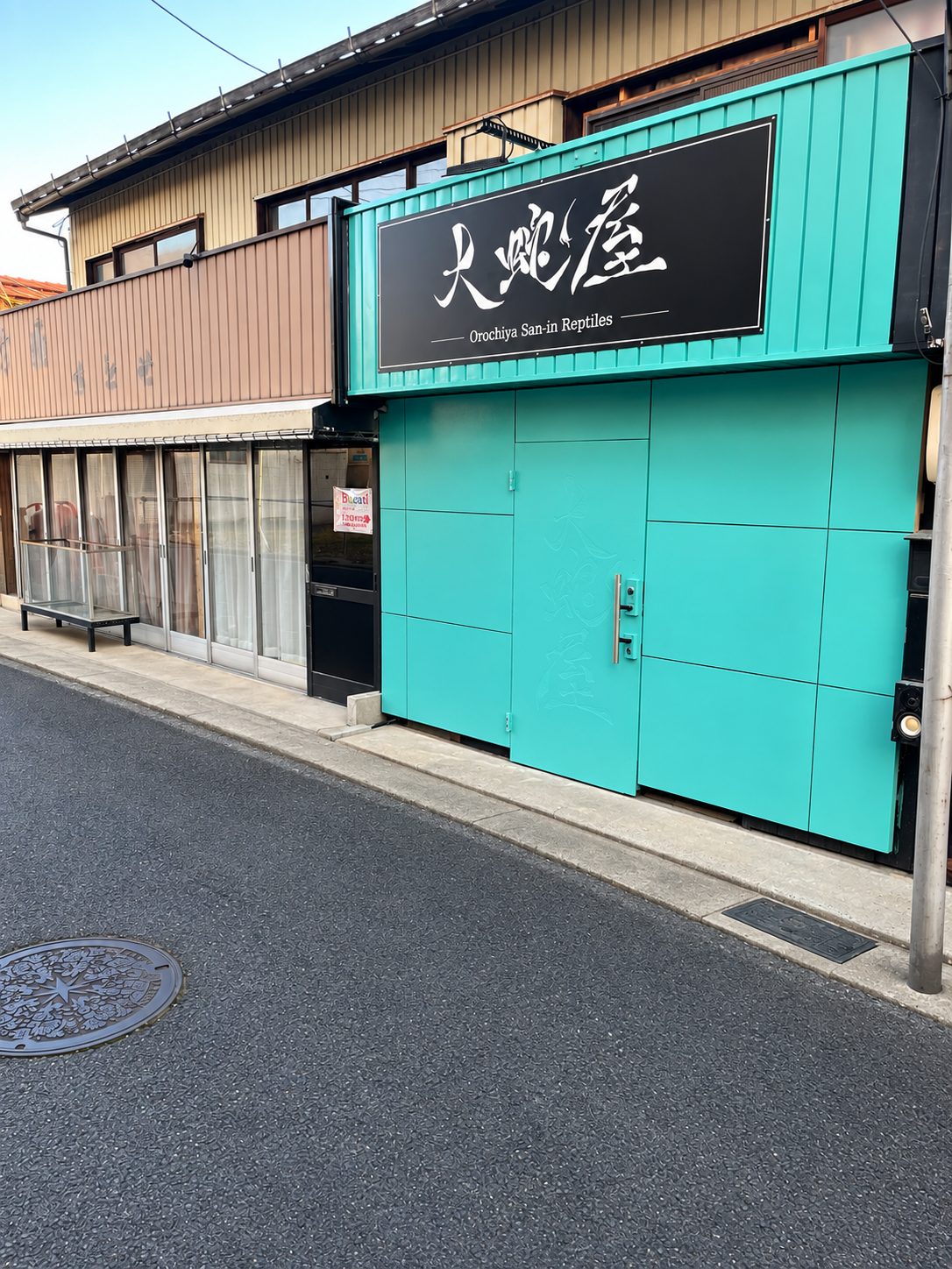 大蛇屋 San-in Reptilesの外観。ターコイズの外壁と黒い看板